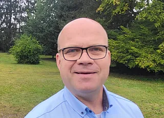 Porträtaufnahme von Pastor Thomas Dietl, mit Bäumen und Rasenfläche im Hintergrund
